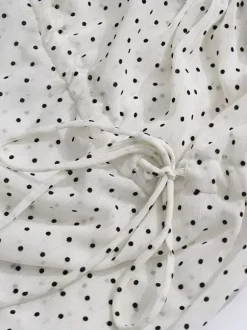Blouse blanche pour femme col en V manches longues lacées et à volants.