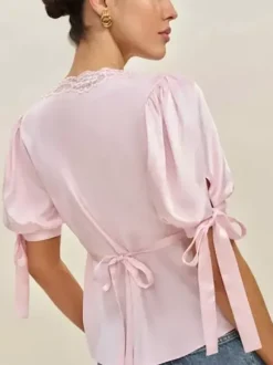 Chemisier en satin à col V bouffant et manches courtes bouffantes orné de dentelle avec ceinture à nouer dans le dos et coupe ajustée. Élégante chemise pour femme.