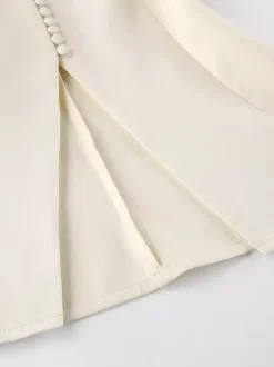 Veste blazer péplum sans manches à col en V et boutonnage nacré à une rangée de boutons.
